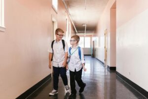 Two boys in school uniforms walking down a bright hallway carrying backpacks. Education concept.