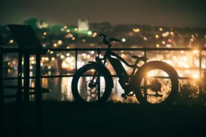 A silhouette of a bicycle with a vibrant city background illuminated by lights at night.